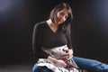 Tranquil Pregnant Caucasian Woman in Supporting Dress. Sitting Against Black Background