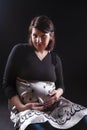 Tranquil Pregnant Caucasian Woman in Supporting Dress. Sitting Against Black Background