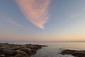 Tranquil seascape at sunset with a pinkish-white cloud in the sky.