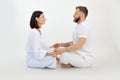 Tranquil sporty family of woman, man sitting with crossed legs, closed eyes on floor, meditating on white background. Royalty Free Stock Photo