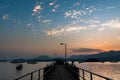 Tranquil sunset scene featuring a pier with silhouetted boats sailing through still waters of a lake