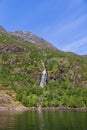 The tranquil waters of Trollfjorden reflect the sunlit, verdant landscape and a thin waterfall descending Royalty Free Stock Photo