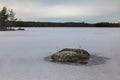 Tranquil winter scenery with a rock in frozen lake