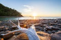 Tranquility beach at sunset. The sun setting on a coastline and old drift log on the rocks beach foregrounds. Laem Son, ranong,