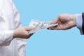 Transfer of a bundle of 100 dollar bills to a female doctor on a blue background. Concept: a bribe to a doctor, payment for treatm Royalty Free Stock Photo