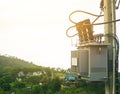 Transformer to supply electricity on cement pole With a house on the mountain as a background