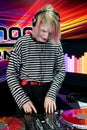 Transgender DJ sets up mixing equipment, with two red records, wears a striped sweatshirt