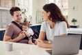 Transgender Family With Baby Working From Home Looking At Laptop On Kitchen Counter