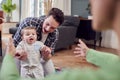 Transgender Family Encouraging Baby To Take First Steps In Lounge At Home