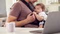 Transgender Father Working From Home On Laptop Looking After Baby Son In Sling Royalty Free Stock Photo