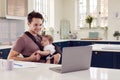 Transgender Father Working From Home On Laptop Looking After Baby Son In Sling Royalty Free Stock Photo