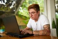 Transgender freelancer works on laptop in tropical coworking space. Focused individual with tattoos tech for remote job