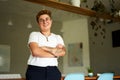 Confident Gen Z individual with tattoos stands in modern office. Transgender young adult smiles, arms crossed, wearing