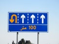 Translation of Arabic (100 M one hundred meters) at a side informative traffic sign board showing 4 lanes and directing
