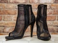 Translucent black summer women`s boots on a white leather banquette against a brick wall