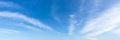 Translucent cirrus cloud stripes float slowly high in a bright blue sky on a sunny day. Panoramic skyscape shot. Weather,