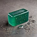 A translucent green bar of soap rests on a textured gray surface, surrounded by scattered water droplets. Royalty Free Stock Photo