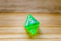 A translucent green eight sided playing dice on a wooden background with number five on a top