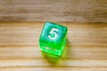 A translucent green six sided playing dice on a wooden background with number five on a top