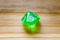 A translucent green ten sided playing dice on a wooden background with number five on a top