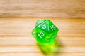 A translucent green twenty sided playing dice on a wooden background with number five on a top