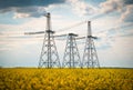 Transmission towers in the middle of a yellow canola field in bloom. High voltage power line at Spring Royalty Free Stock Photo