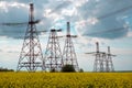 Transmission towers in the middle of a yellow canola field in bloom. High voltage power line at Spring Royalty Free Stock Photo