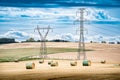 Transmission towers and power lines overlooking a farm fields with round hay bales on the Canadian prairies in Royalty Free Stock Photo