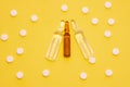 Transparent ampoules with liquid medicine are on yellow background around tablets which form polka dots pattern. Concept photo of