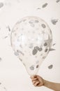 Transparent balloon with stars and silver confetti in the hands of a woman isolated on white