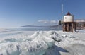 Transparent blue ice hummocks on lake Baikal shore. Siberia winter landscape view with lighthouse. Snow-covered ice of