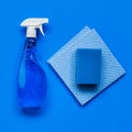 Transparent blue sprayer with window cleaner, rags and sponge on blue background. Royalty Free Stock Photo