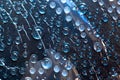 Transparent blue and white raindrops flow down on the glass  surface of a blue background. Royalty Free Stock Photo