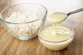 Transparent bowl with cottage cheese, tspoon with condensed milk above bowl with milk on wooden table Royalty Free Stock Photo