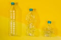 Transparent and crushed plastic bottles with blue caps on a yellow background. Recycling and environment concept Royalty Free Stock Photo