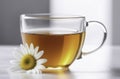 A transparent cup with chamomile tea on light white table. There are chamomile flowers nearby. Royalty Free Stock Photo