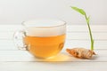 Transparent cup with hot tea, wet from steam on glass, dry ginger root with green sprout next to it. Royalty Free Stock Photo