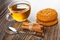 Cup with tea, oat cookies with sunflower seeds, cinnamon sticks, spoon on wooden table
