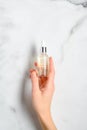 Transparent dropper bottle with serum lotion or essential oil in female hand over marble table. Skin care cosmetics concept