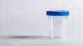 Transparent empty urine analysis container with a blue lid. Clear specimen cup on a white backdrop. Concept of