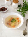 Transparent fish soup with vegetables and percussion in a white bowl on a white plate.