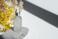 Transparent frosted glass dropper bottle with serum, tonic or essential oil on grey concrete podium with yellow flowers. Royalty Free Stock Photo