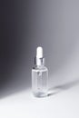 Transparent glass bottle with silver and white pipette in light on grey background mockup. Facial serum in dropper Royalty Free Stock Photo