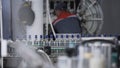 Transparent glass bottles sealed with blue foil and filled with alcohol move along conveyor line with control panel in Royalty Free Stock Photo