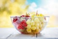 Transparent glass bowl filled with freshly picked strawberries and grapes, washed in water. Blurry bright sky and trees Royalty Free Stock Photo