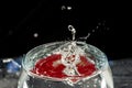 Transparent glass bowl, filled with water, with red reflection and splashing drops. Splash Effect Royalty Free Stock Photo