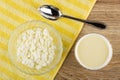 Transparent bowl with cottage cheese, spoon on napkin, bowl with condensed milk on wooden table. Top view Royalty Free Stock Photo