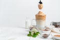 Transparent glass with coffee and milk dessert and a spoon with cream on a white background.