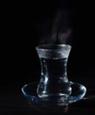 Transparent glass cup with swell the boiling water into it. The vapor from the top. Black background.