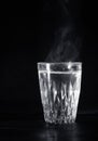 Transparent glass cup with swell the boiling water into it. The vapor from the top. Black background. Royalty Free Stock Photo